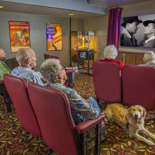 A group of seniors enjoying a classic movie in a cozy home theater setting, accompanied by a dog.