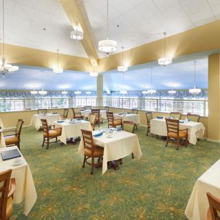 A spacious restaurant dining area with neatly arranged tables and chairs, large windows, and elegant lighting.