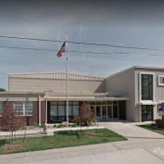 A view of a school building featuring an American flag and landscaped grounds.