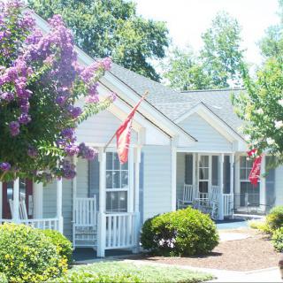A row of charming suburban houses with porches and flags, surrounded by trees on a sunny day.