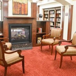 A cozy library setting with armchairs around a fireplace and bookshelves in the background.
