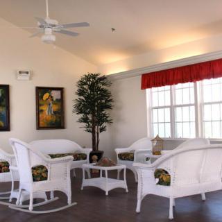 A cozy living room featuring white wicker furniture, decorative artwork, and ample natural light.