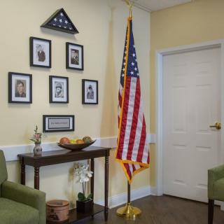 A room decorated with an American flag, framed photos, and a small table against a light-colored wall.