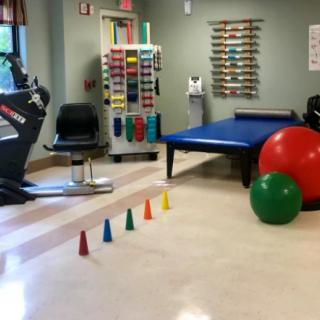 A physical therapy room equipped with various exercise tools, including an exercise bike, colorful cones, and large balls.