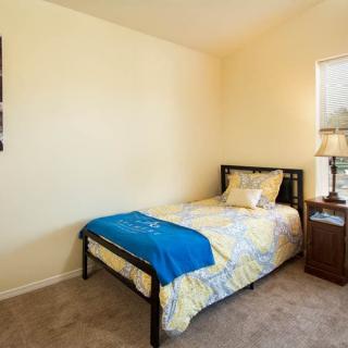A cozy bedroom featuring a single bed with colorful bedding and a blue throw blanket, accompanied by a wooden nightstand with a lamp near a window.