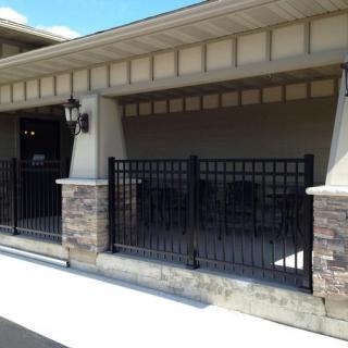 A building exterior featuring a stone wall and a black metal fence enclosing a small patio area.