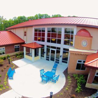 A building with a red roof featuring glass windows and outdoor seating on a landscaped patio.