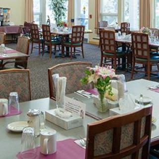 A well-lit dining room with neatly arranged tables and chairs, featuring flowers as decor.