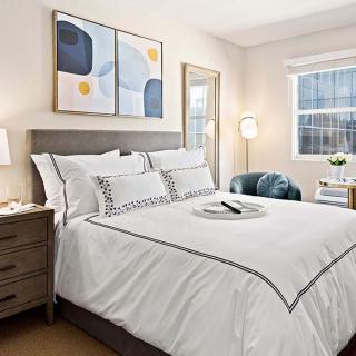 A modern bedroom with white bedding and contemporary decor, illuminated by natural light.