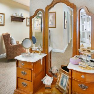 An elegant wooden vanity table with a three-panel mirror in a cozy bedroom setting.