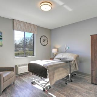 A modern hospital room featuring a patient bed, comfortable furniture, and natural light from the window.