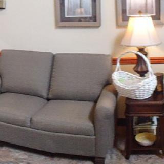 A cozy living room corner featuring a gray sofa, side table with a lamp and decorative basket.