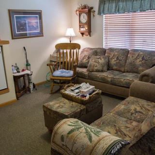 A cozy living room with a patterned sofa, ottoman, and a rocking chair near a wall clock.