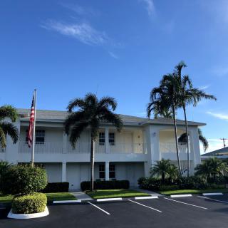 A white building with palm trees and a flagpole under a clear blue sky.