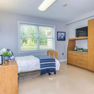 A clean and minimalist hospital room featuring a single bed, a window, and a television.