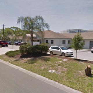 A view of a commercial building with parking and palm trees in the foreground.