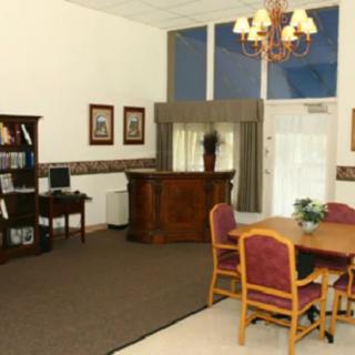 A well-lit room with a desk, chairs, bookshelf, and chandelier.