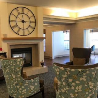 A cozy living room featuring a stylish clock and comfortable chairs around a fireplace.