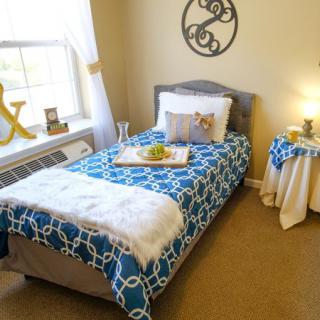A cozy bedroom with a single bed adorned with a blue patterned blanket, complemented by soft lighting and decor.