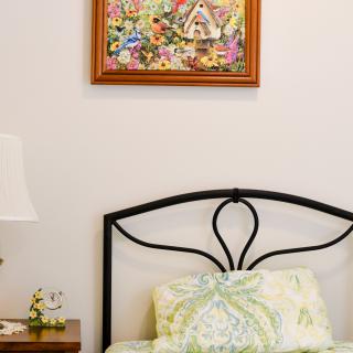 A cozy bedroom with a metal headboard, decorative pillows, a bedside lamp, and a colorful painting on the wall.