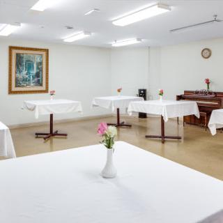 A serene and well-lit room featuring elegantly set dining tables, a decorative piano, and a touch of floral decor.