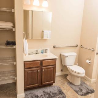 A clean and organized bathroom with a sink, toilet, mirror, and shelving unit with towels.