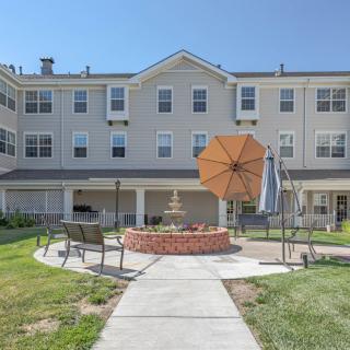 A sunny courtyard with outdoor seating and umbrellas in front of a multi-story residential building.