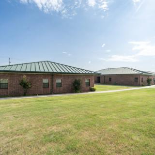 Two brick buildings with green roofs surrounded by a grassy lawn under a blue sky.