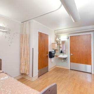 A clean and well-organized hospital room featuring a bed, curtain for privacy, and essential amenities.