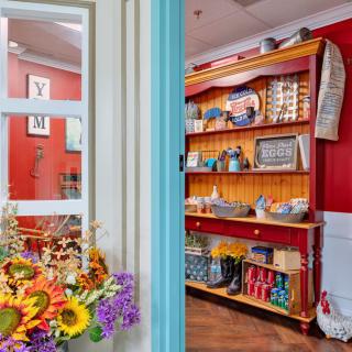 A cozy cafe interior with bright red walls, colorful flowers, and vintage-style shelves filled with various items.