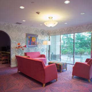 A cozy living room with modern furniture, including red sofas and a coffee table, illuminated by a chandelier and natural light from large windows.