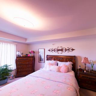 A cozy bedroom with a warm ambiance, featuring a neatly made bed, decorative pillows, dressers, and soft lighting.