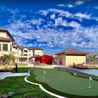 Scenic view of a putting green surrounded by buildings under a bright, cloudy sky.