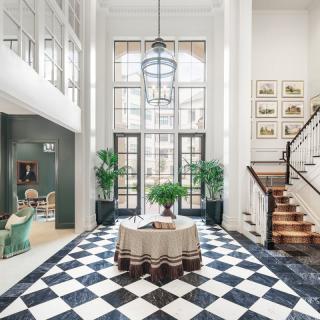 A luxurious foyer with a grand staircase and checkered floor, illuminated by abundant natural light.