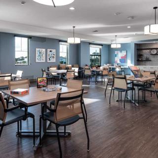A modern dining area with neatly arranged tables and chairs, featuring soft lighting and a hardwood floor.