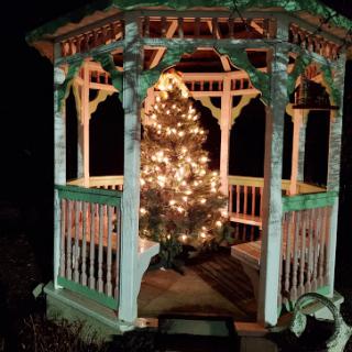 A beautifully decorated gazebo featuring a glowing Christmas tree, creating a festive atmosphere on a serene night.