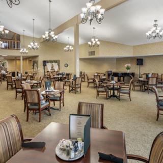 A spacious dining area with multiple tables and chairs, illuminated by elegant chandeliers.