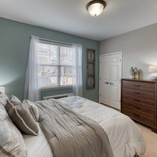 A cozy and modern bedroom featuring a neatly made bed, a dresser, and soft lighting with natural light streaming in through a window.