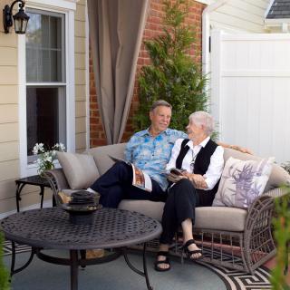 A couple relaxing on a patio sofa while reading books.