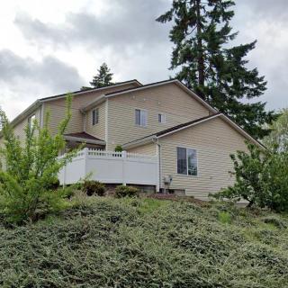A suburban house surrounded by greenery and trees, featuring a white fence.