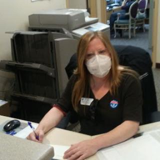 A woman wearing a mask diligently working at an office desk.