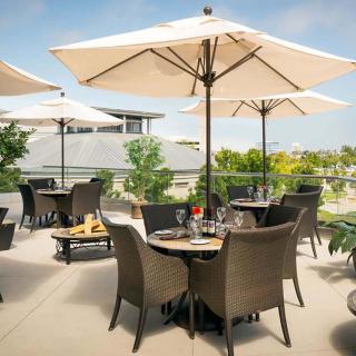 A sunny outdoor restaurant patio with tables, chairs, and umbrellas.