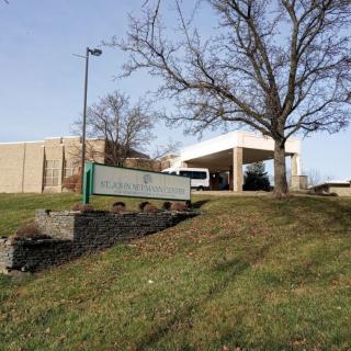 A hospital building with a green lawn and a large tree nearby.