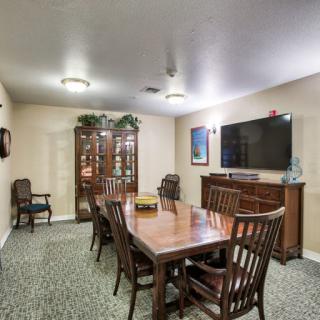 A well-furnished dining room with a large table, chairs, cabinet, and wall-mounted television.