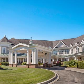 A large estate with a circular driveway and well-maintained landscaping under a clear blue sky.
