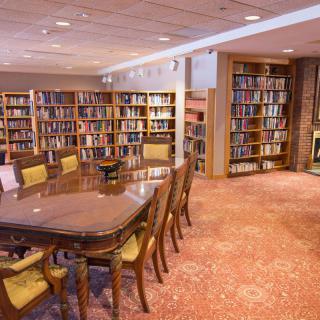 A cozy library reading room with bookshelves, a large table, and chairs.