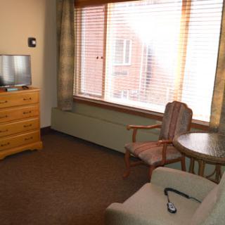 A cozy living room setup featuring a dresser, television, chair, and large window.