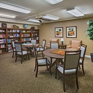 A cozy library room with multiple tables and chairs, surrounded by bookshelves and decorated with wall art.
