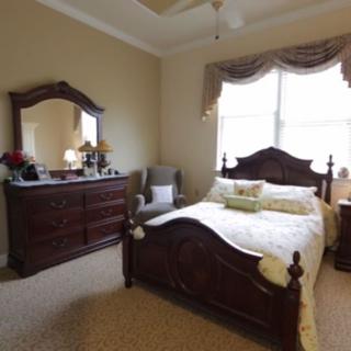 A traditional-style bedroom with a wooden bed and matching dresser, featuring a large window allowing natural light.