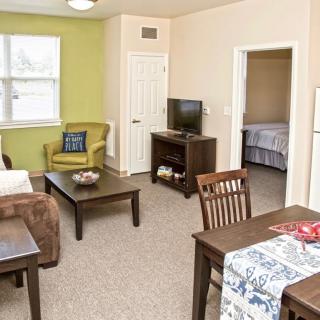 A cozy apartment living room with a television, coffee table, and dining area.